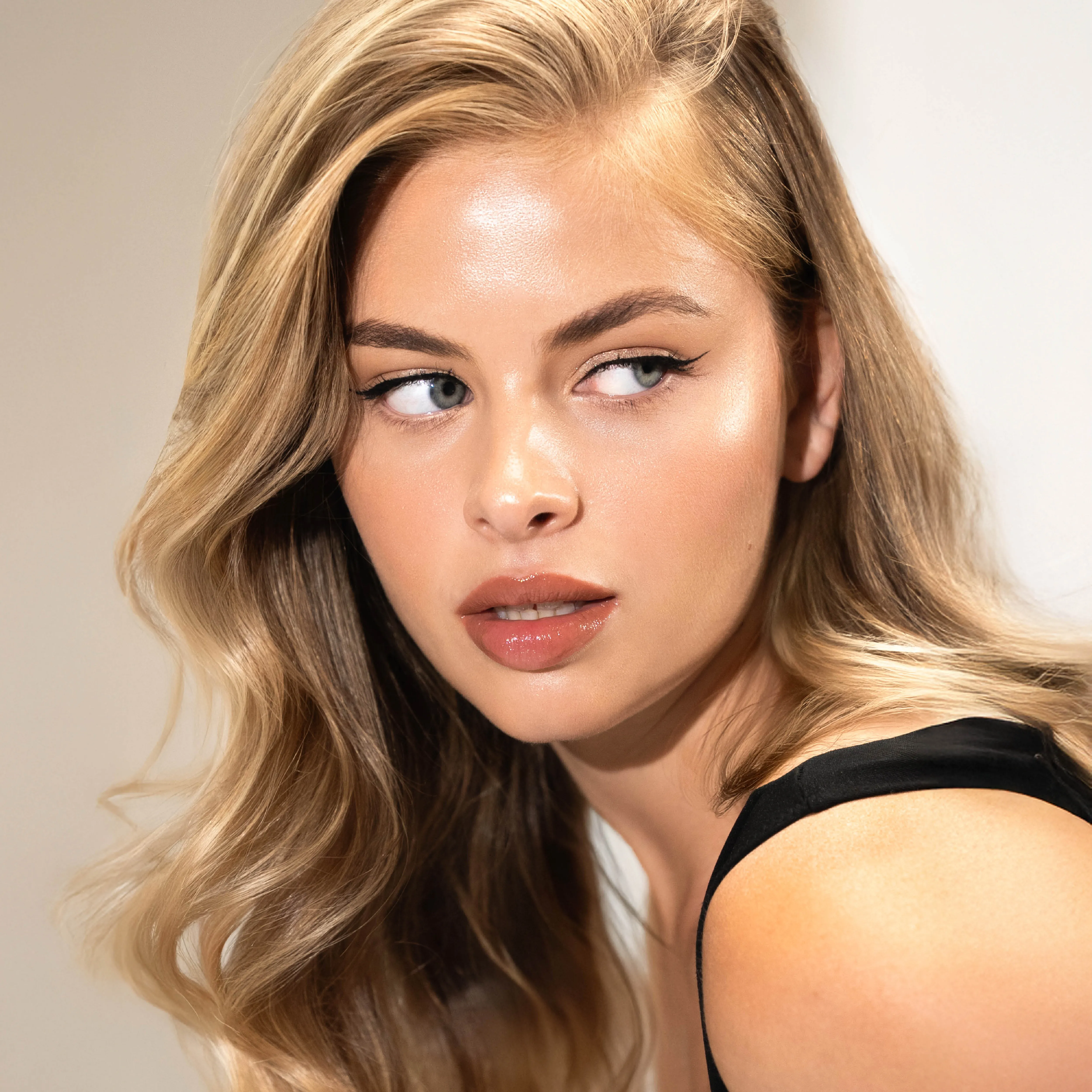 Porträt einer Frau mit langen, glänzenden, blond-beigen Wellen und seitlichem Scheitel als Inspiration für einen eleganten, geschmeidigen Blowout-Look.