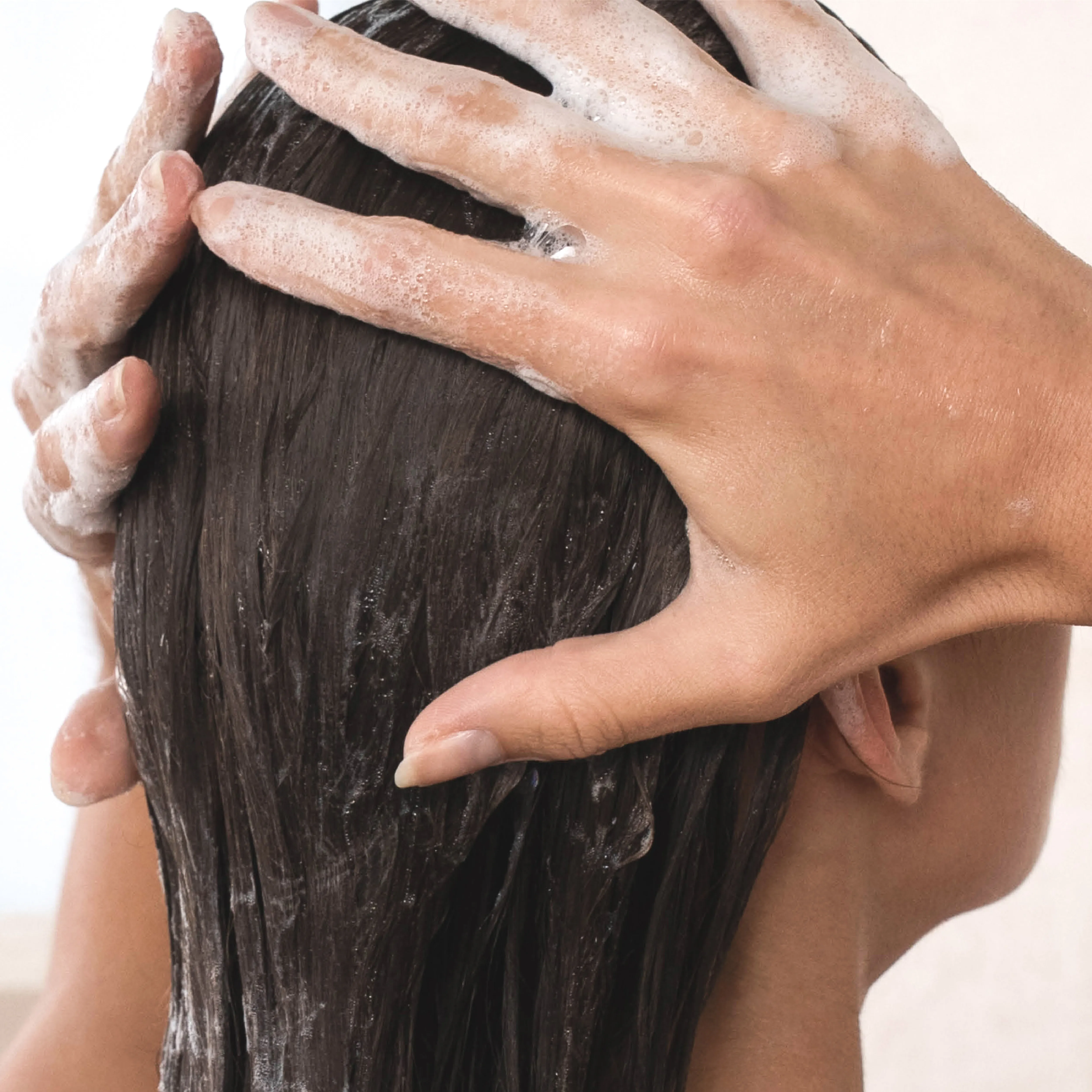 Eine Frau massiert Shampoo in die Kopfhaut ein und reinigt ihr Haar gr&uuml;ndlich w&auml;hrend der Haarw&auml;sche.